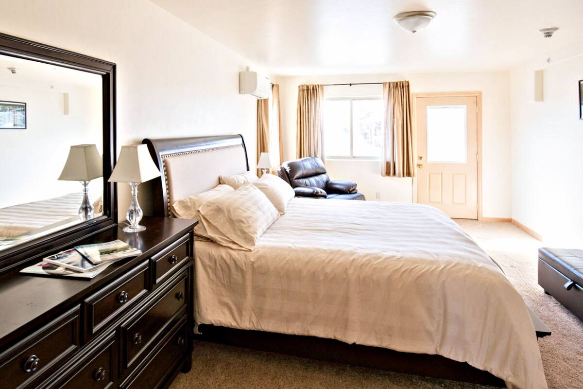 A hotel room with a large bed, a dresser with a mirror, a desk with a lamp, and a chair.