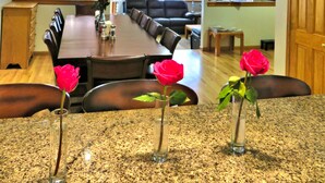 A dining area with a long table, chairs, and vases with flowers. There are hanging lights above the table. - Mein Haus Bed & Breakfast (Avon)