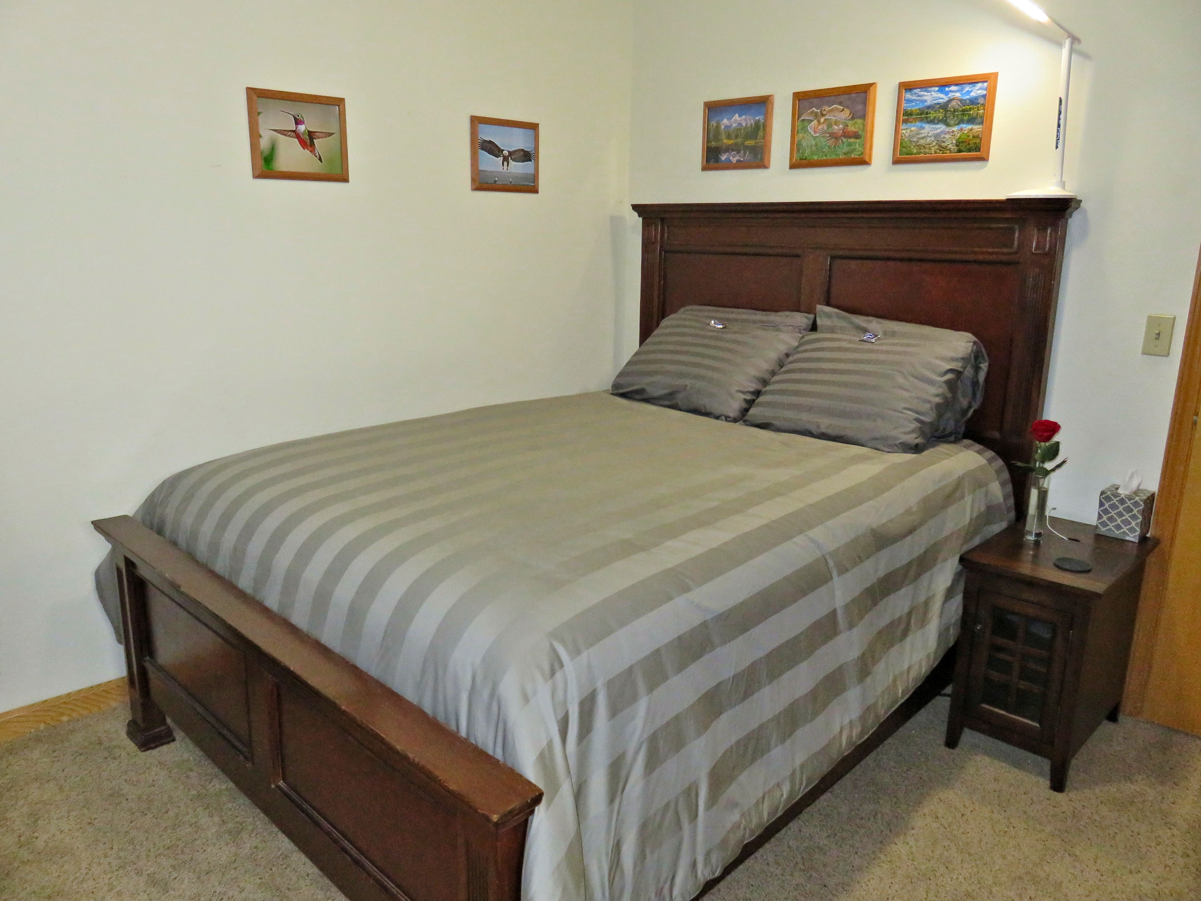 A bedroom with a bed, a nightstand, and three framed pictures on the wall.