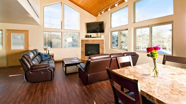 A spacious living room with a fireplace, leather sofas, a dining table, and large windows offering a view of the outdoors. - Mein Haus Bed & Breakfast (Avon)
