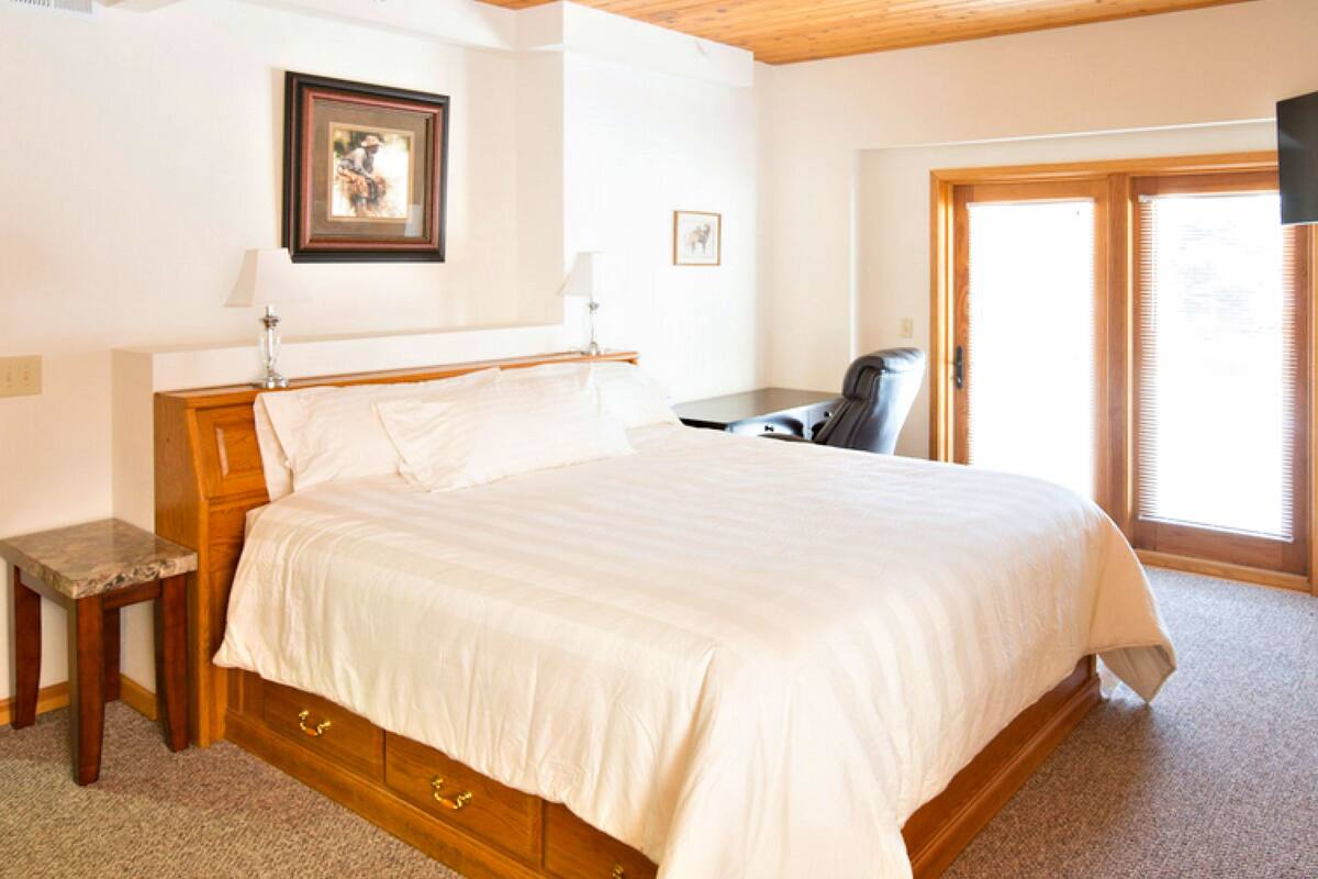 A bedroom with a large bed, wooden headboard, a desk, and a chair.