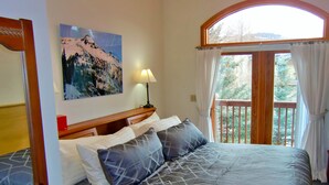 A bedroom with a bed, a nightstand, a lamp, a painting, and a view of the outdoors. - Mein Haus Bed & Breakfast (Avon)