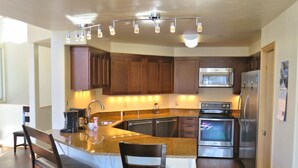 A modern kitchen with granite countertops, stainless steel appliances, wooden cabinets, and a central island with seating. - Mein Haus Bed & Breakfast (Avon)