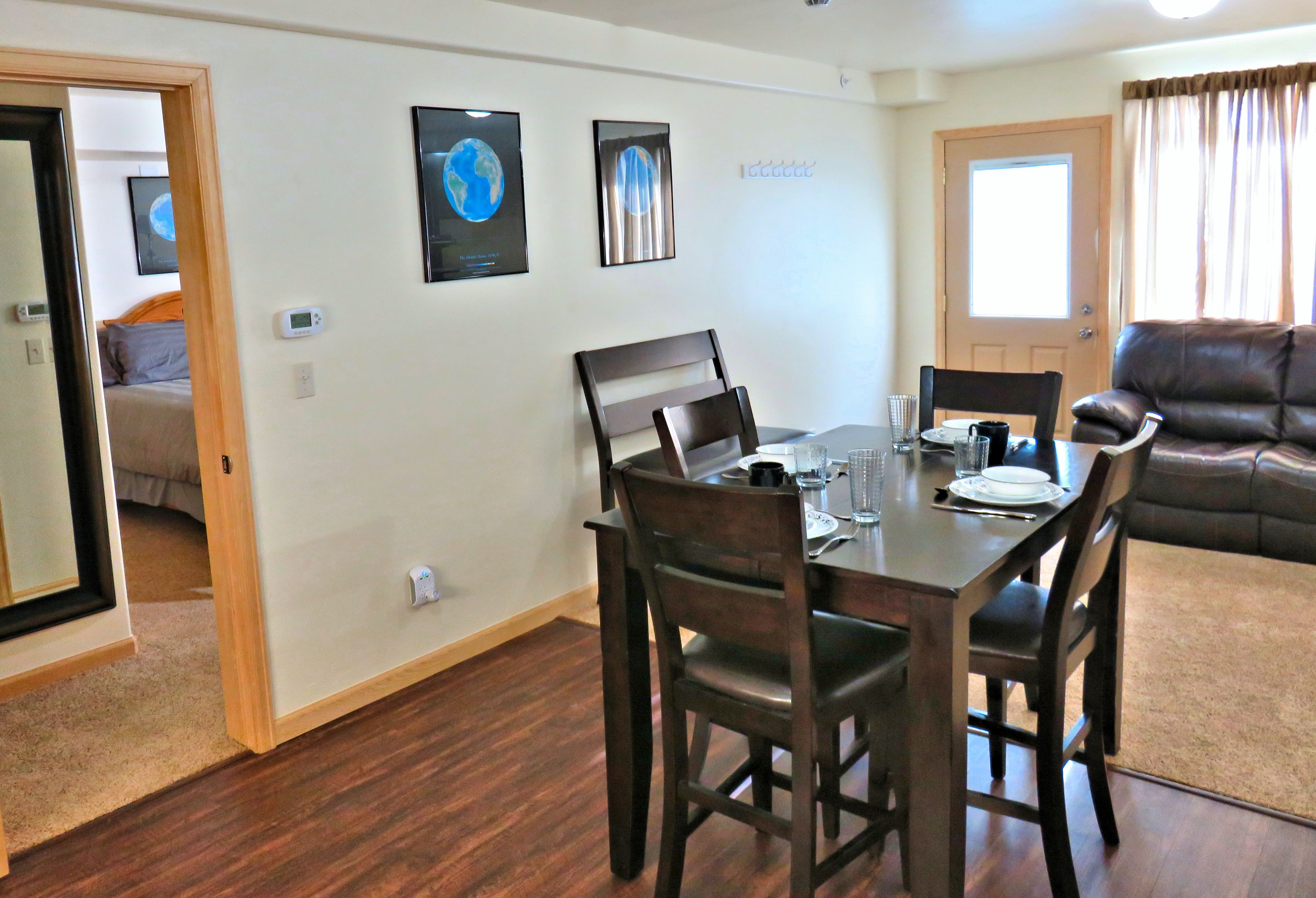 A dining area with a wooden table and chairs, a sofa, and a door leading to another room.