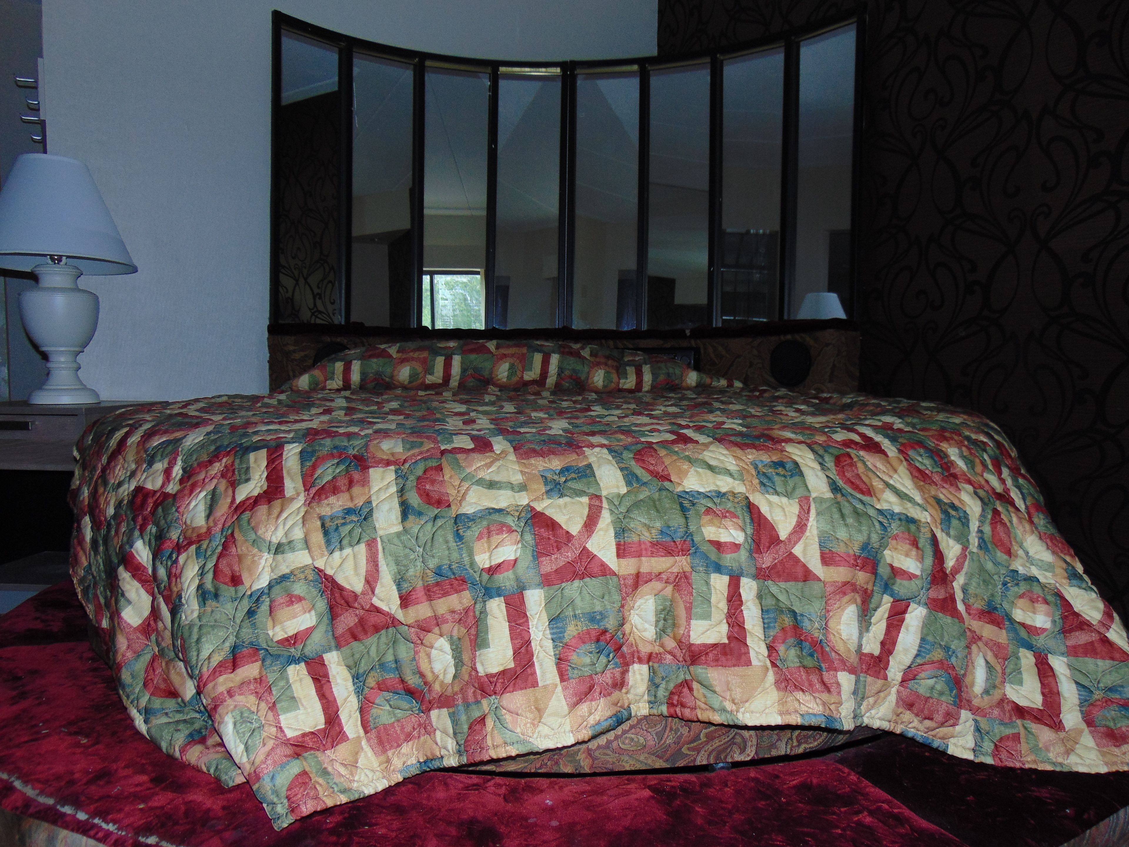 A bedroom with a large bed, a curved headboard, and a mirror above the bed.