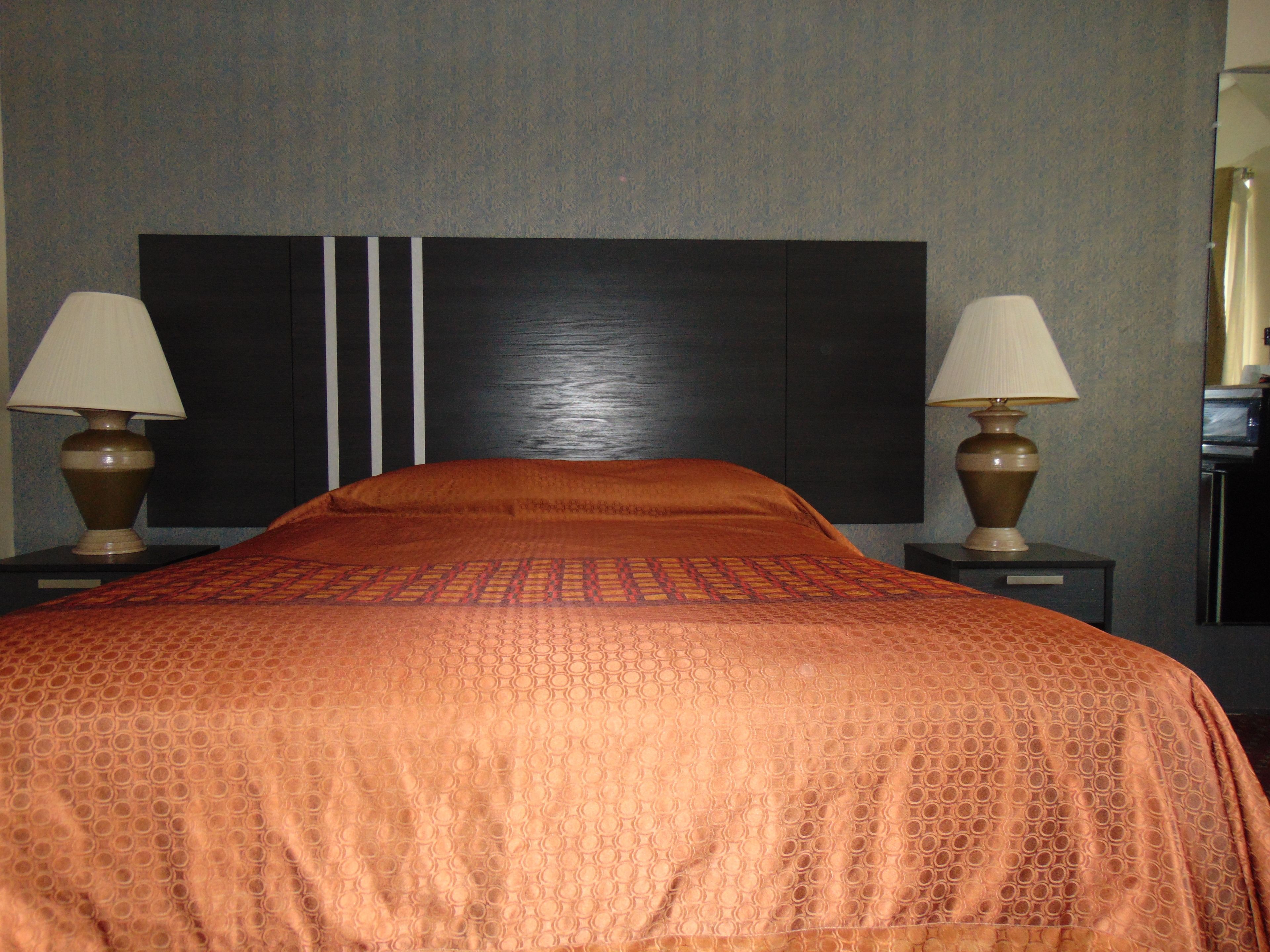 A hotel room with a large bed, two bedside lamps, and a dark headboard.
