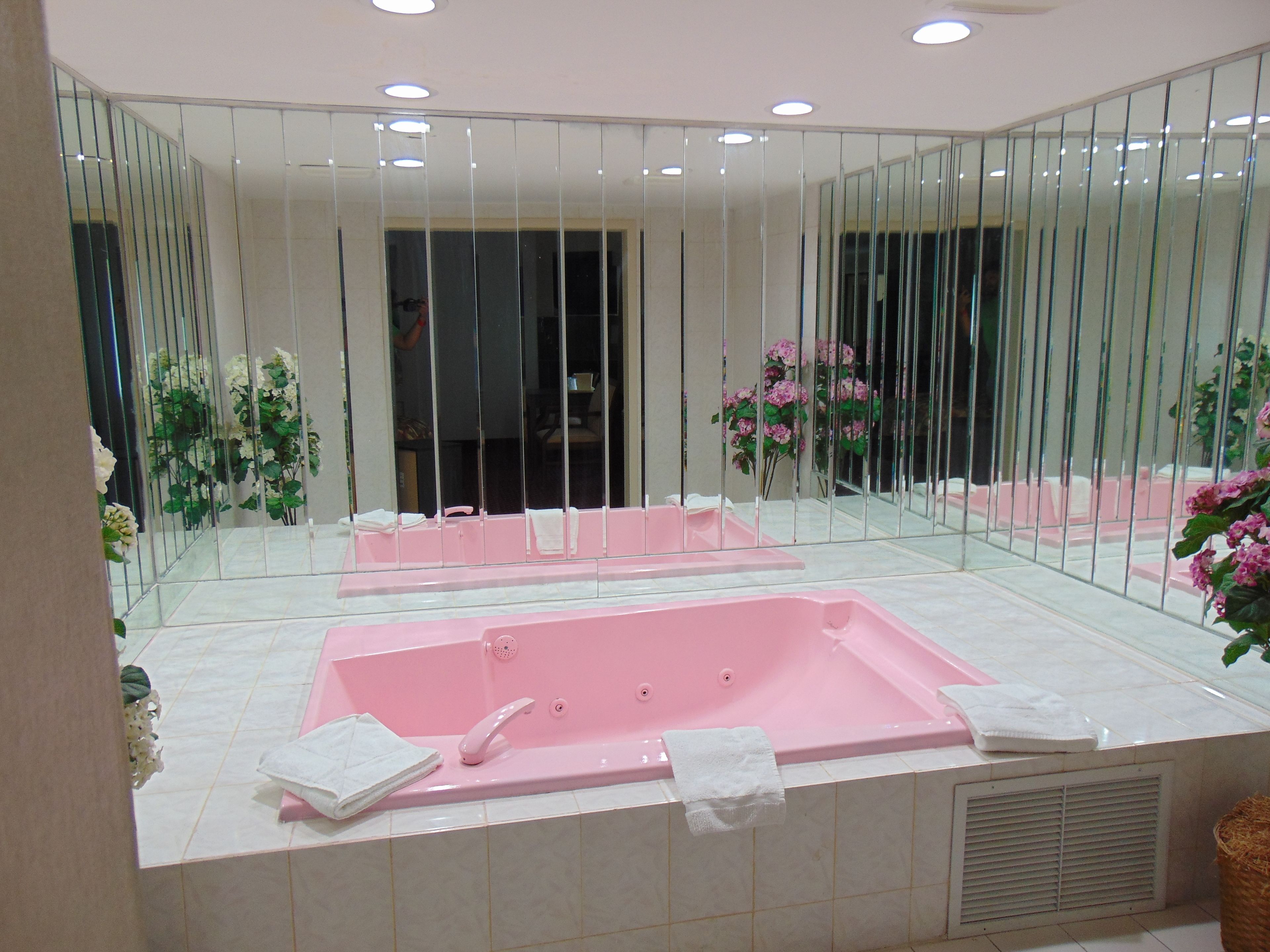 A modern bathroom with a large mirror, a pink bathtub, and white tiles.