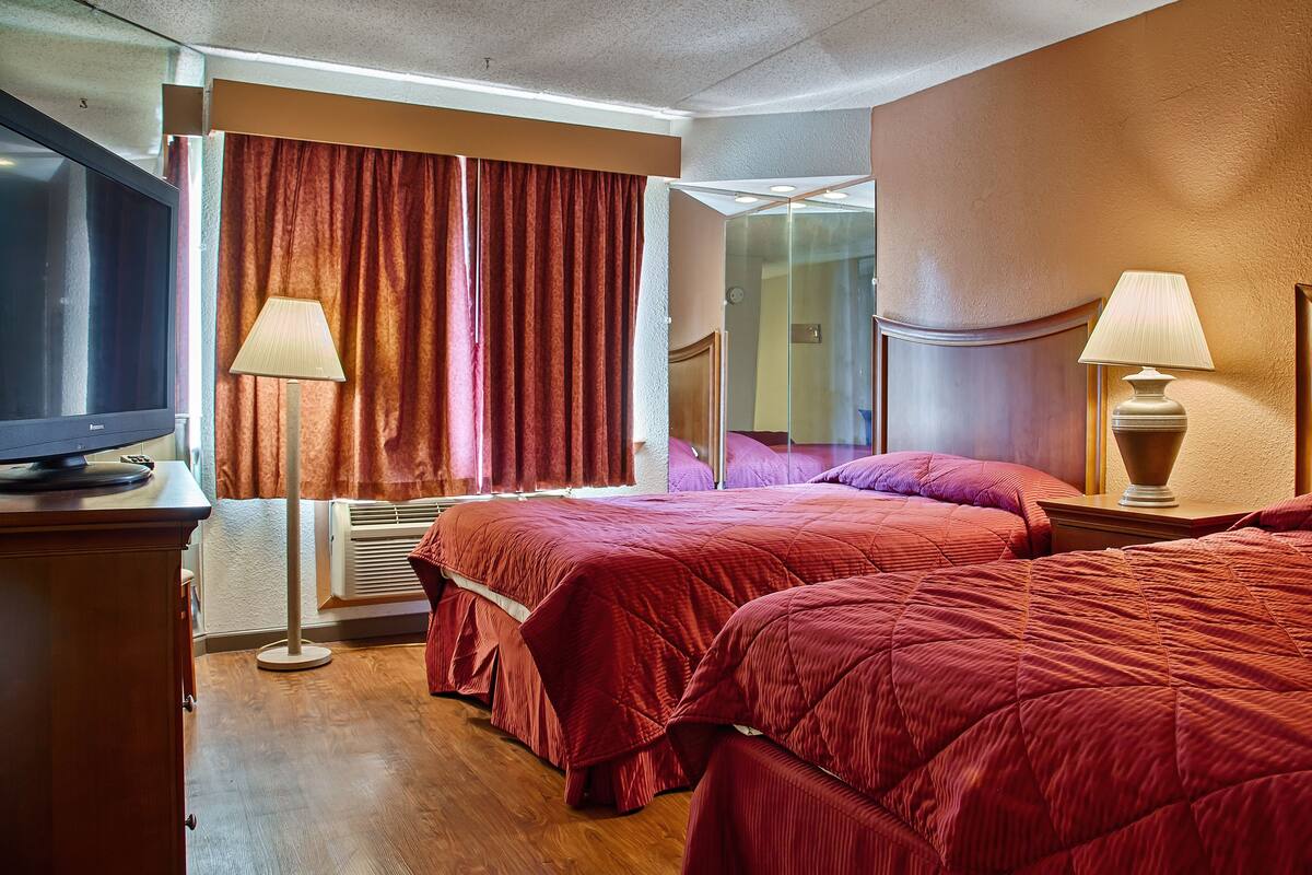 Habitación de hotel con dos camas, un televisor, un espejo y una ventana con cortinas.
