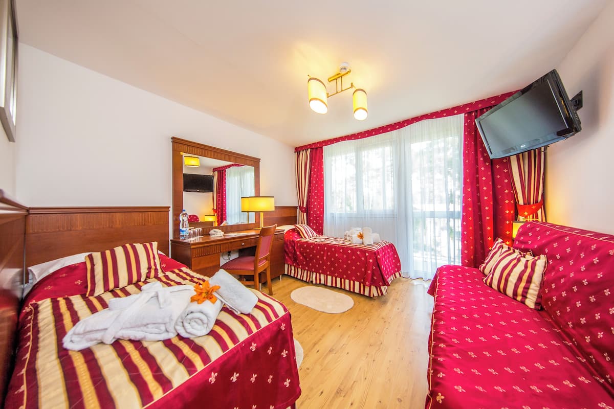 Habitación de hotel con dos camas, un escritorio, una silla, un televisor montado en la pared y un ventanal con cortinas.