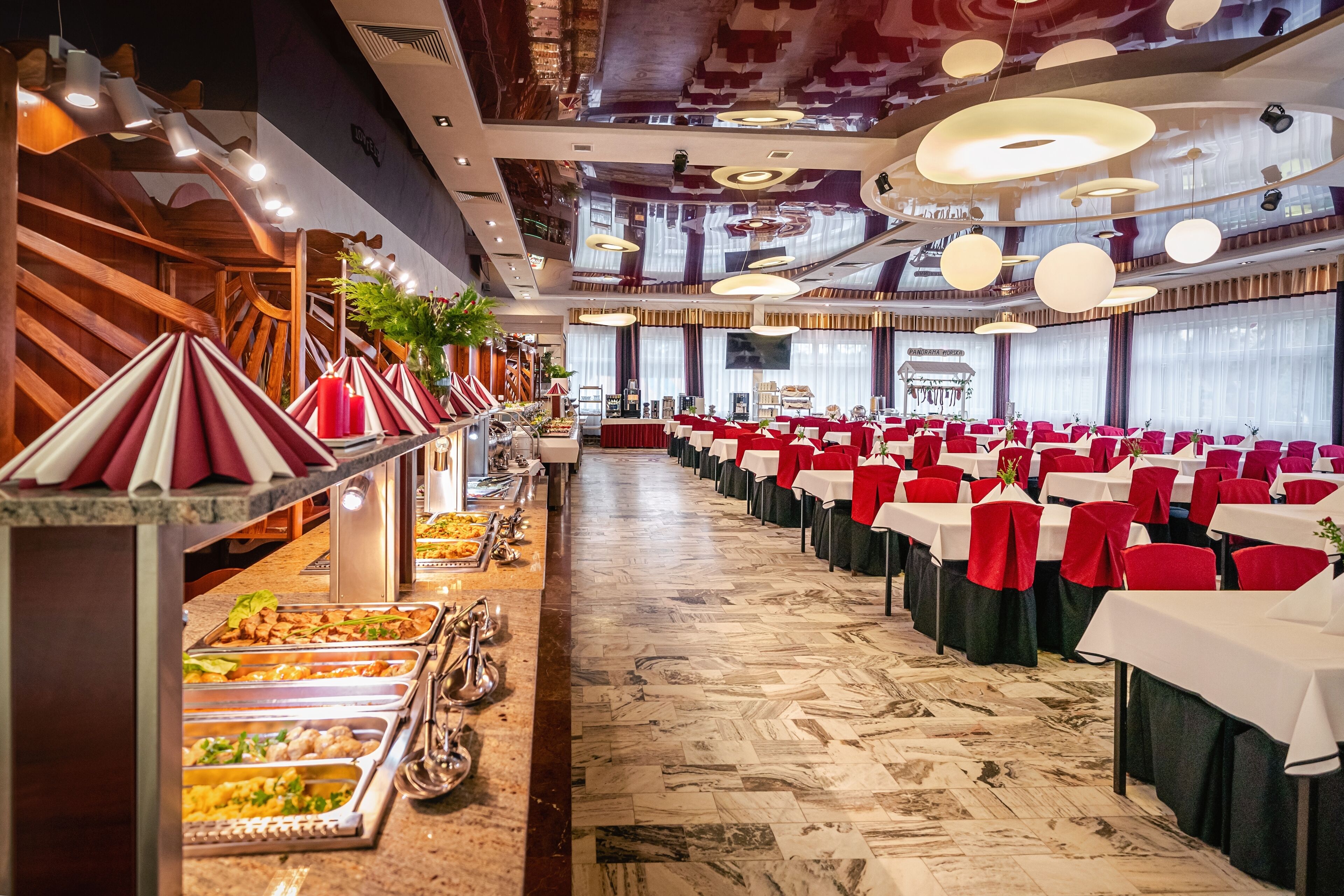 A banquet hall with rows of tables, a buffet area, and a stage in the background.