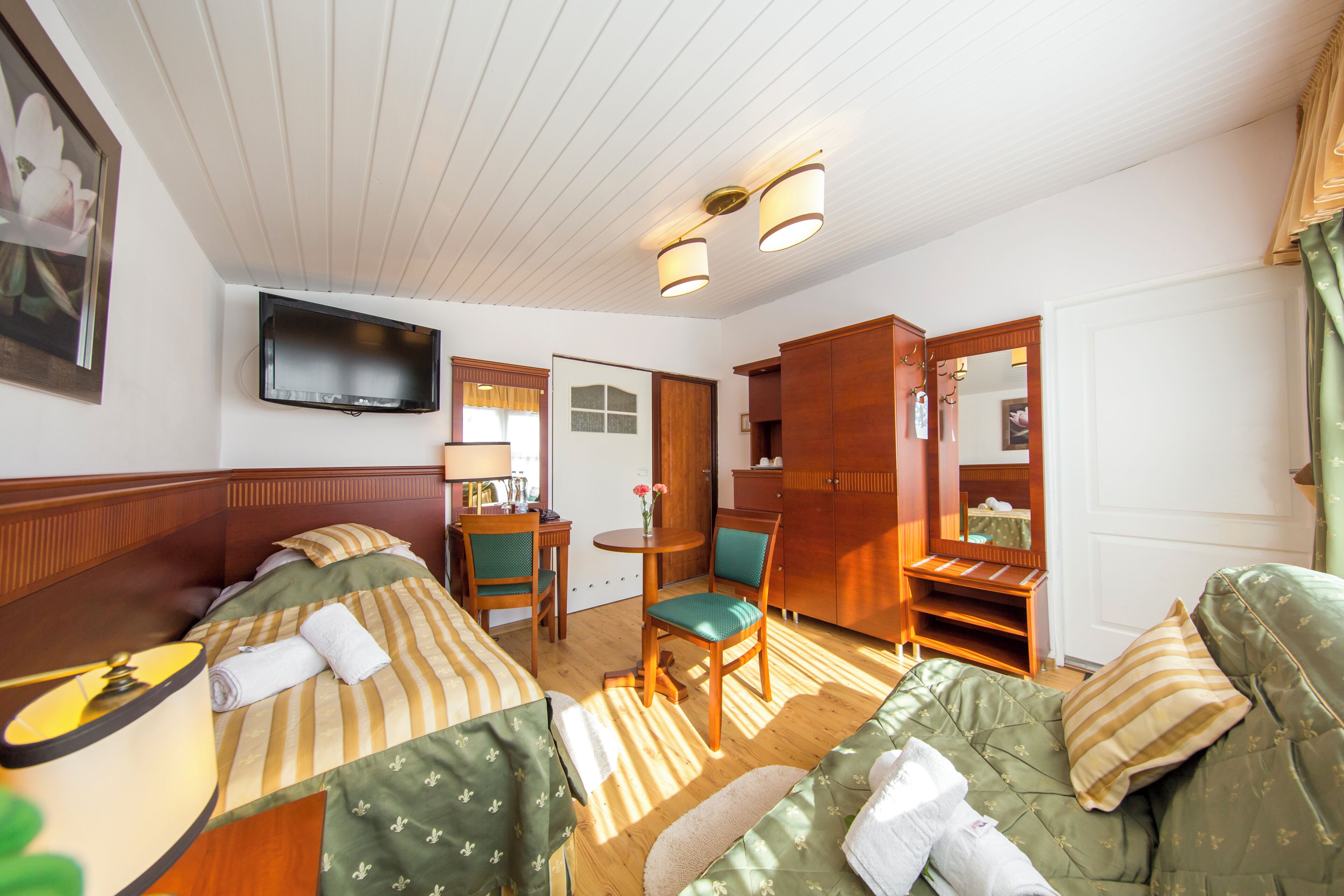 Ein Hotelzimmer mit zwei Betten, einem Fernseher, einem Schreibtisch mit Stuhl, einem Spiegel und einem Kleiderschrank.