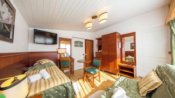 Ein Hotelzimmer mit zwei Betten, einem Fernseher, einem Schreibtisch mit Stuhl, einem Spiegel und einem Kleiderschrank.