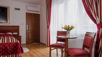 Habitació d'hotel amb un llit, una nit de fusta, una taula rodona amb un ram de flors, dues cadires vermelles i una porta de fusta.