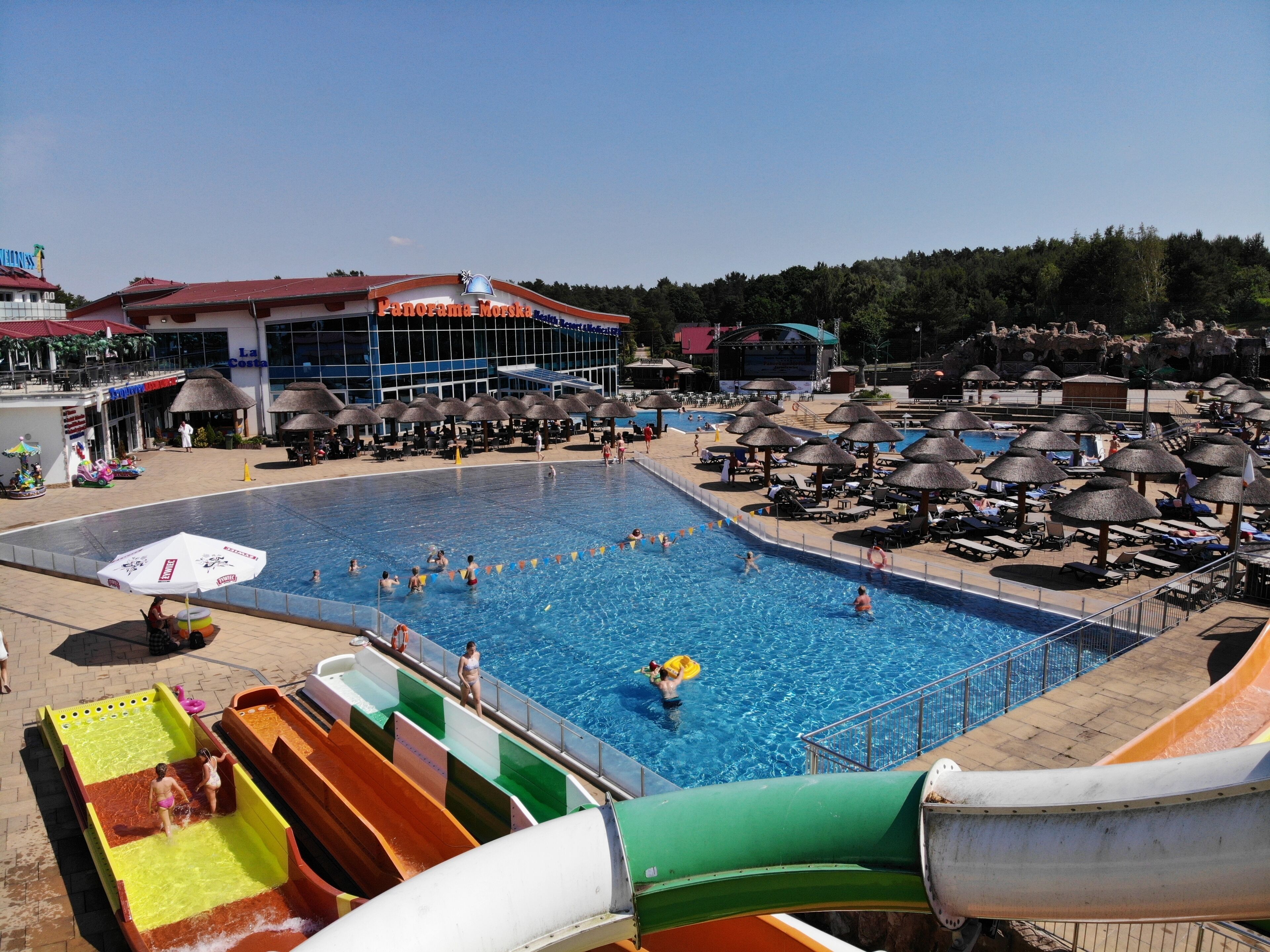 Zona de piscina con toboganes, sombrillas y sillones reclinables.