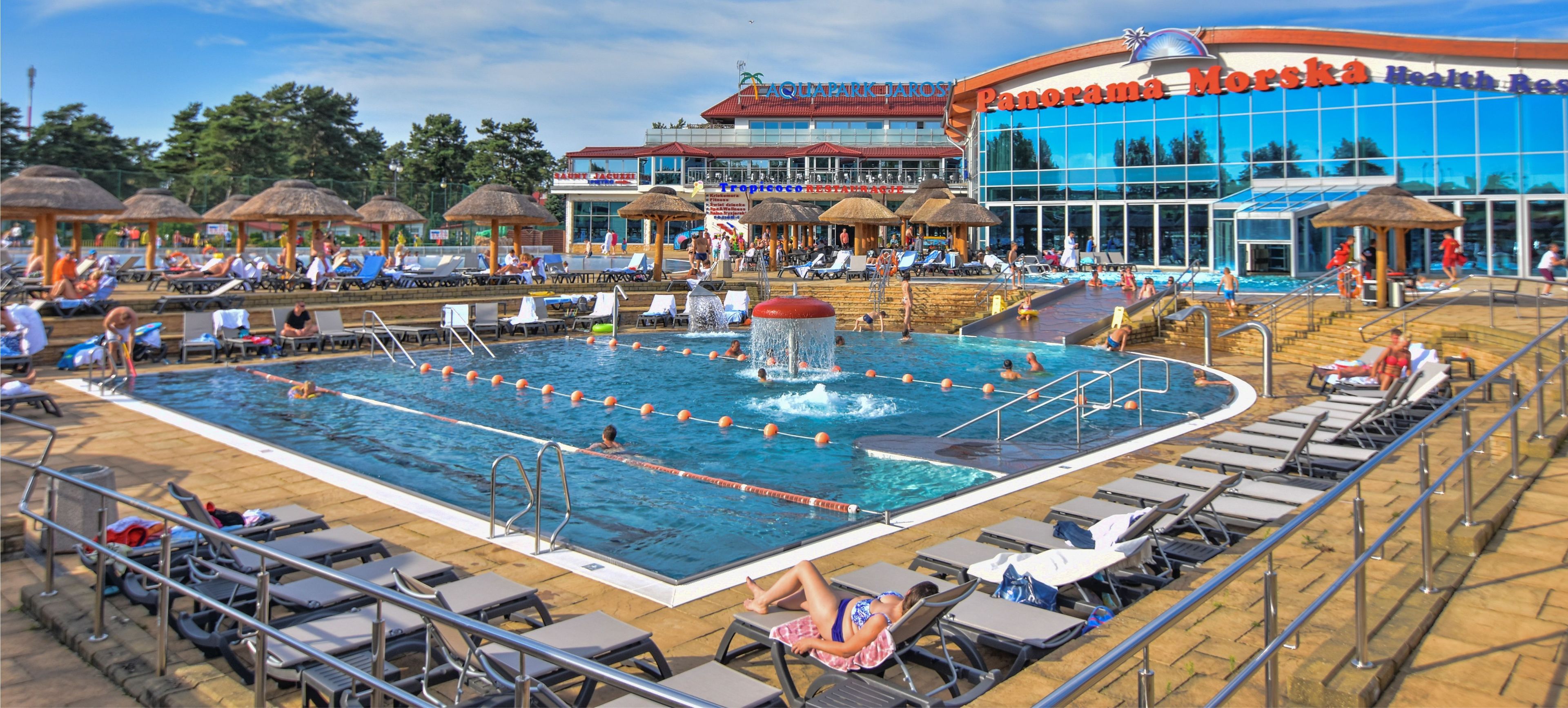 A large outdoor swimming pool with multiple lanes, sun loungers, and a water slide.