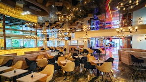 Un restaurant spacieux doté de plusieurs espaces de restauration, de lustres modernes et offrant une vue sur le paysage urbain grâce à de grandes fenêtres.