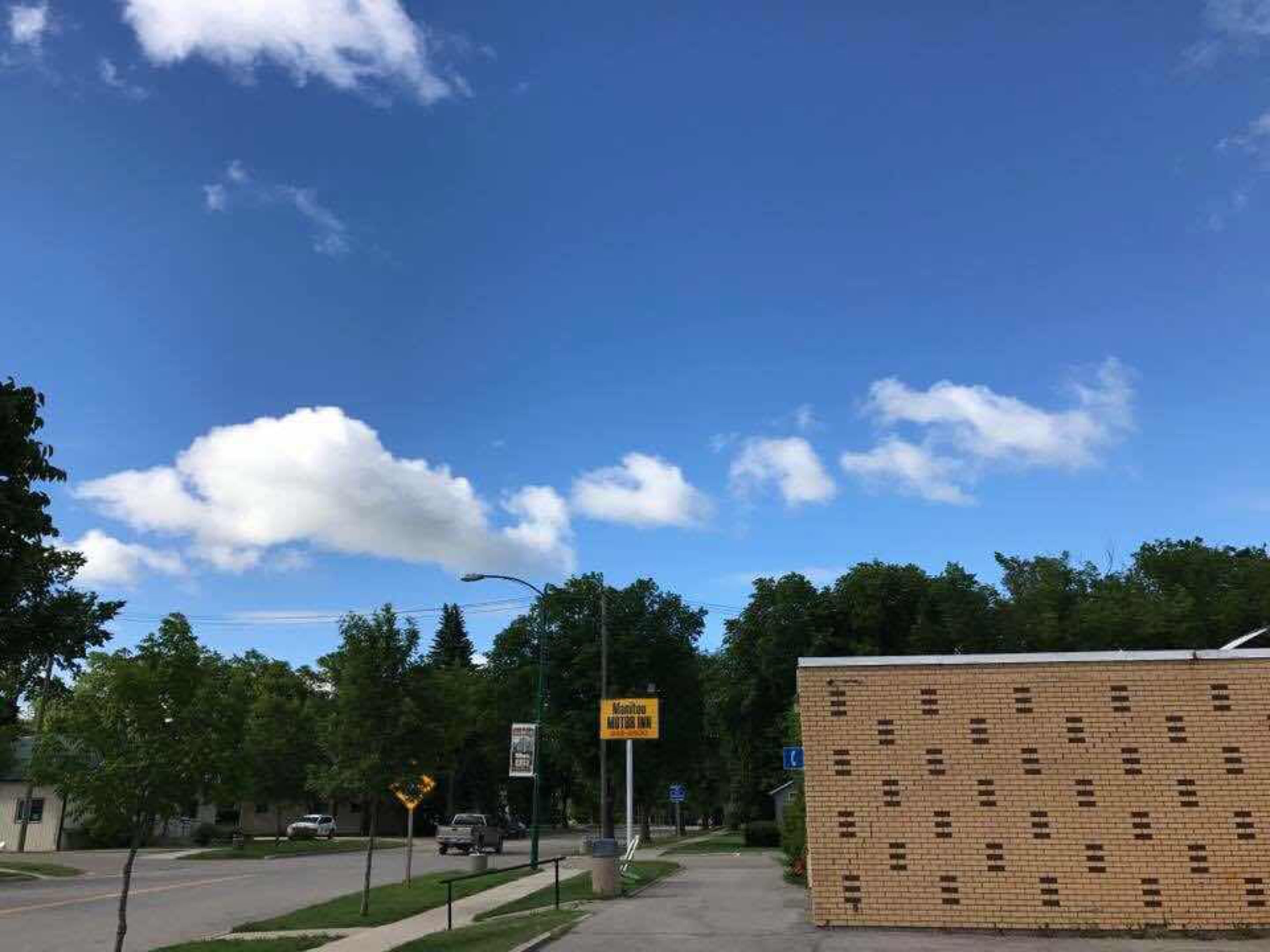A street view with a brick building, a clear blue sky, and a few clouds.