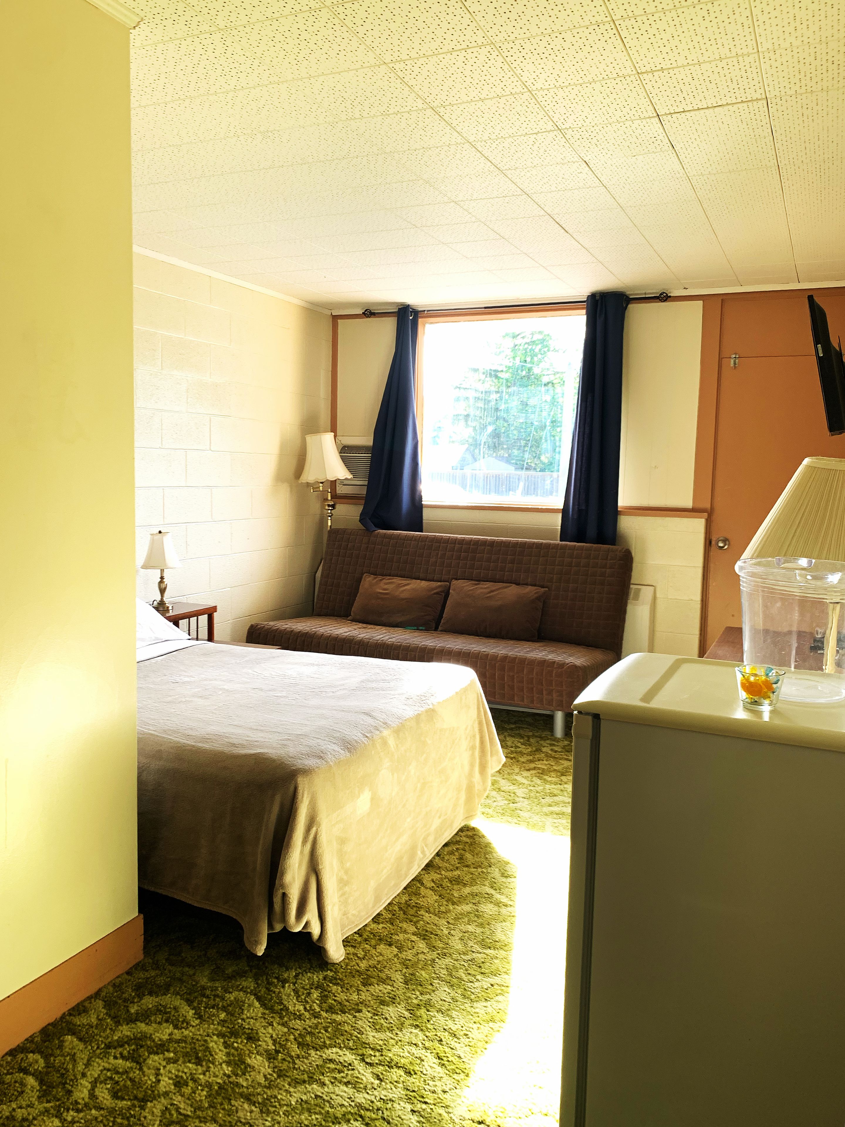 A hotel room with a bed, a sofa, a desk, and a window with curtains.