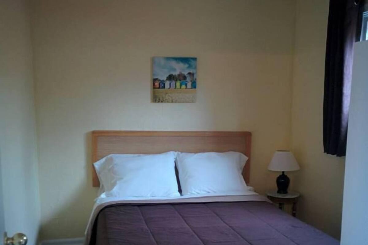 A hotel room with a bed, a nightstand with a lamp, a ceiling fan, and a painting on the wall.