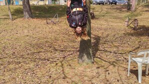 A person hanging upside down from a tree in a wooded area with a chair nearby. - The Pinewood - Adult Getaway by the Lake (Lambton Shores)
