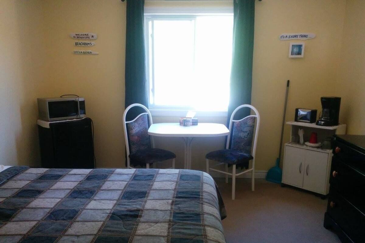 A hotel room with a bed, a small table with two chairs, a TV, a cabinet, and a window with curtains.