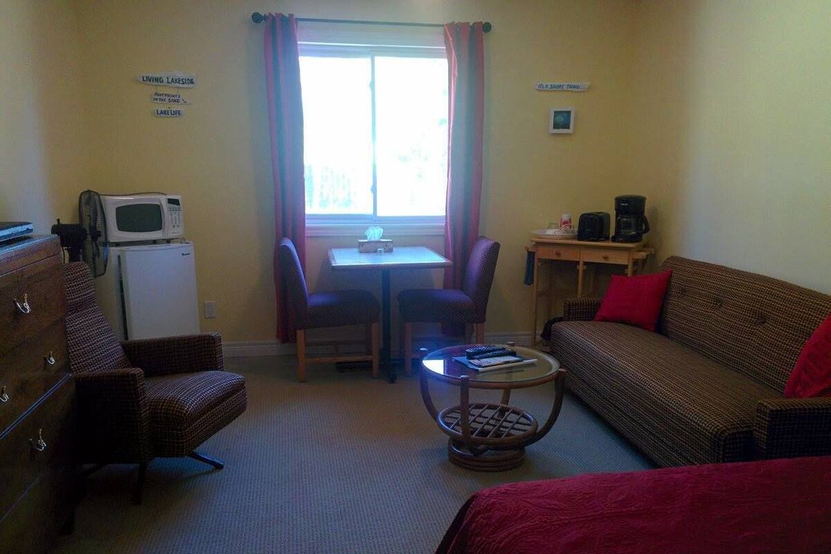 A small, furnished room with a sofa, a chair, a table, a microwave, and a small cabinet.
