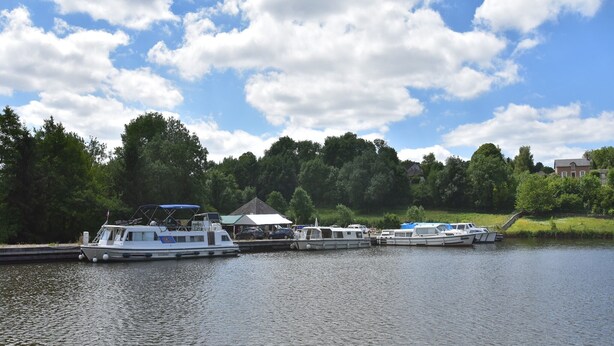 A marina with several boats docked, a small building with a green roof, and a backdrop of trees and houses. - Holiday Home in Crux-la-Ville near Lake (Crux-La-Ville)