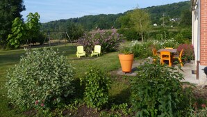 A patio with outdoor seating, a garden with various plants, and a view of a hilly landscape. - Holiday Home in Crux-la-Ville near Lake (Crux-La-Ville)