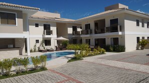 A modern multi-story building with a swimming pool, outdoor seating, and a well-maintained garden. - Residencial Portinari (Porto Seguro)