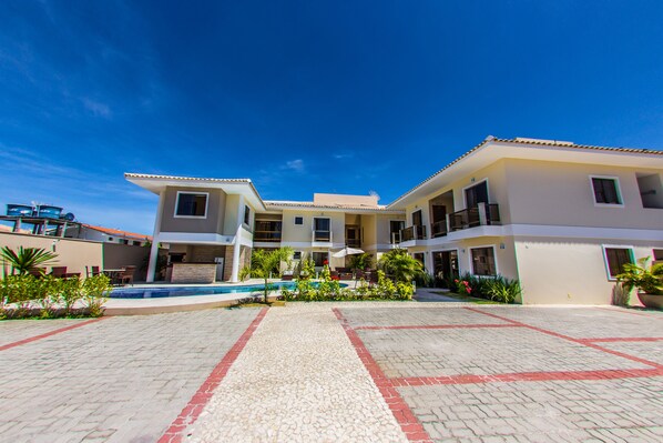 A hotel with a swimming pool, multiple balconies, and a paved courtyard. - Residencial Portinari (Porto Seguro)