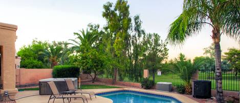 A swimming pool with a tiled edge, surrounded by a patio area with lounge chairs and a hot tub.