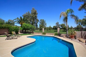 Una piscina de borde curvo, rodeada por una terraza con dos sillas de descanso.