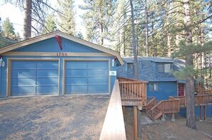 Two-car garage with a staircase leading to a second level, set amidst a serene natural landscape with tall pine trees.