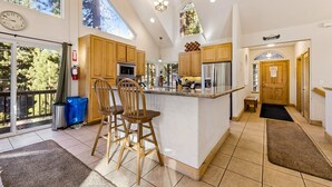 A spacious kitchen with wooden cabinets, a large island with bar stools, a clock, and a view of trees through the windows.