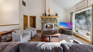 A living room with a stone fireplace, a television, and a large window with a view of trees.