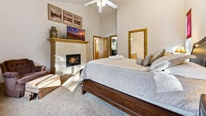 A bedroom with a fireplace, a bed, a chair, and a ceiling fan.