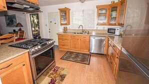 Una cocina con armarios de madera, estufa, lavaplatos, fregadero y microondas.