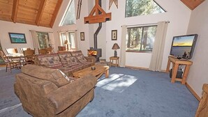 Una sala de estar acogedora con un sofá marrón grande, una mesa de centro y una chimenea. Hay cuadros enmarcados en las paredes y un televisor sobre un mueble de madera.