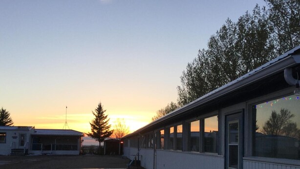 En bygning med et stort åbent område foran, en overdækket sektion med vinduer, og en klar himmel med solnedgang i baggrunden.