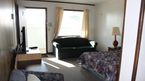 Et hotelværelse med seng, sofa, skrivebord med computer og et vindue med gardiner.