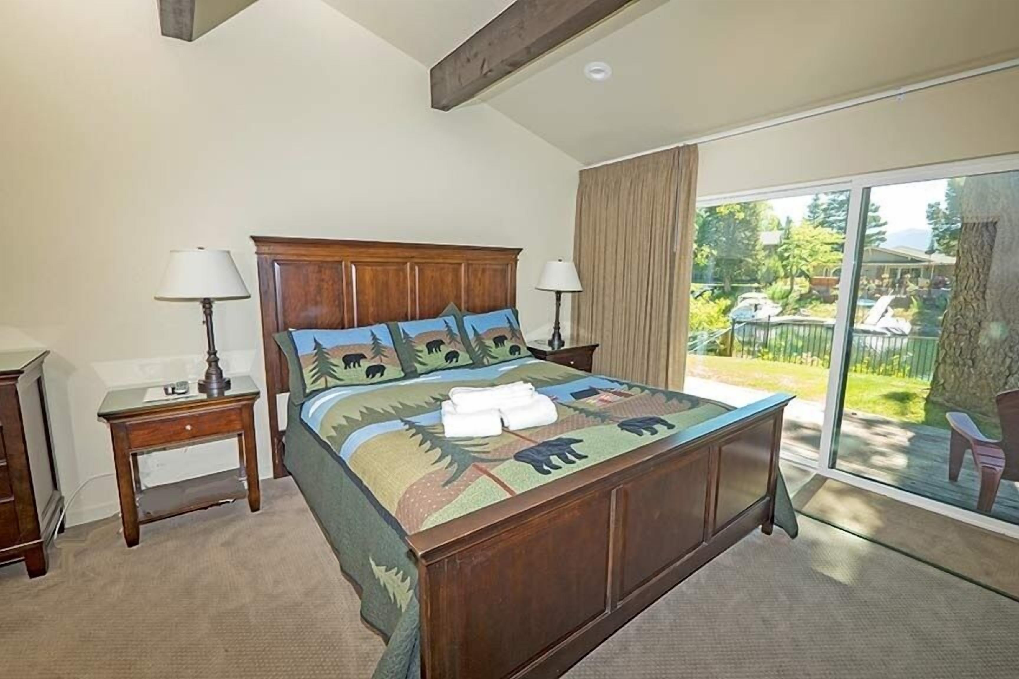 A bedroom with a large bed, two bedside tables, a window with a view of the outdoors, and a ceiling with exposed beams.