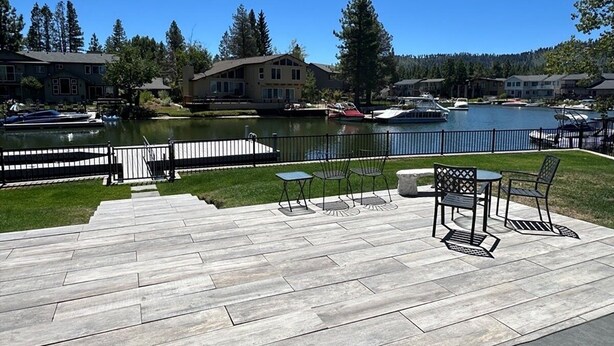 A wooden deck with outdoor furniture, a lake, and houses in the background. - 2130 Monterey Drive 4 Bedroom Home by RedAwning (South Lake Tahoe)