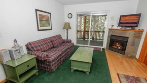 A living room with a plaid sofa, a green coffee table, a fireplace, and a television on a mantel. - 2460 Lupine Trail 6 Bedroom Home by RedAwning (South Lake Tahoe)