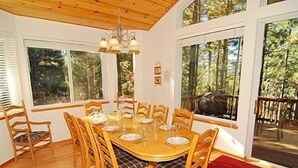 A dining area with a wooden table and chairs, large windows, and a chandelier. - 2460 Lupine Trail 6 Bedroom Home by RedAwning (South Lake Tahoe)