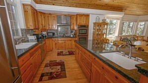 A spacious kitchen with wooden cabinets, granite countertops, a built-in oven, and a large island with a sink. - 2460 Lupine Trail 6 Bedroom Home by RedAwning (South Lake Tahoe)
