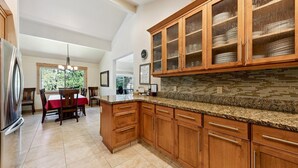 A kitchen with wooden cabinets, a granite countertop, and a dining area with a red tablecloth.