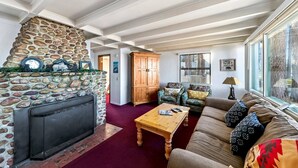 A cozy living room with a stone fireplace, wooden furniture, and a large window.