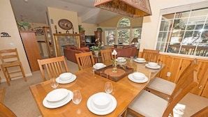 A dining area with a wooden table set for six, surrounded by wooden chairs.