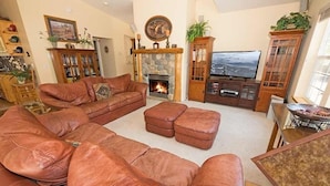 A living room with a large leather sofa, a fireplace, a television, and a dining area.