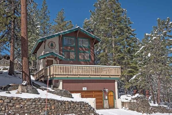 A lodge with a wooden exterior, a balcony, and a stone wall in a snowy forest setting.